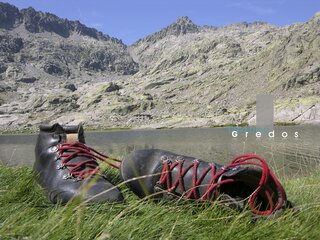 Un par de botas de montaña están sobre hierba, con un paisaje montañoso de fondo en la Sierra de Gredos.