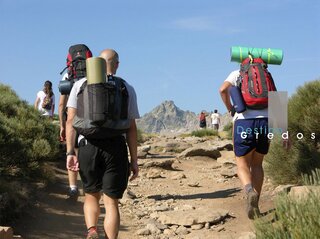 Tres personas caminan por un sendero rocoso en un terreno montañoso en la Sierra de Gredos.