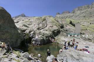 A group of people are relaxing on a rocky surface, likely a mountain slope, with a view of the surrounding rocks en la Sierra de Gredos.