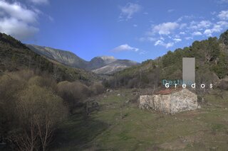 Un paisaje de montaña con un camino sinuoso que se adentra en la distancia. El terreno es verde y cubierto de árboles y arbustos. El cielo es azul en la Sierra de Gredos.